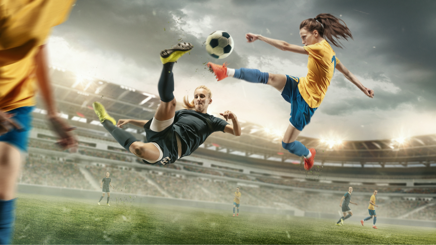 women in soccer field about to kick soccer ball in air