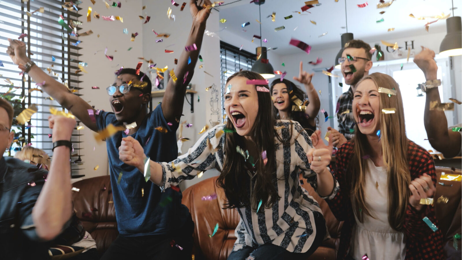group of people cheering in living room with confetti falling in air
